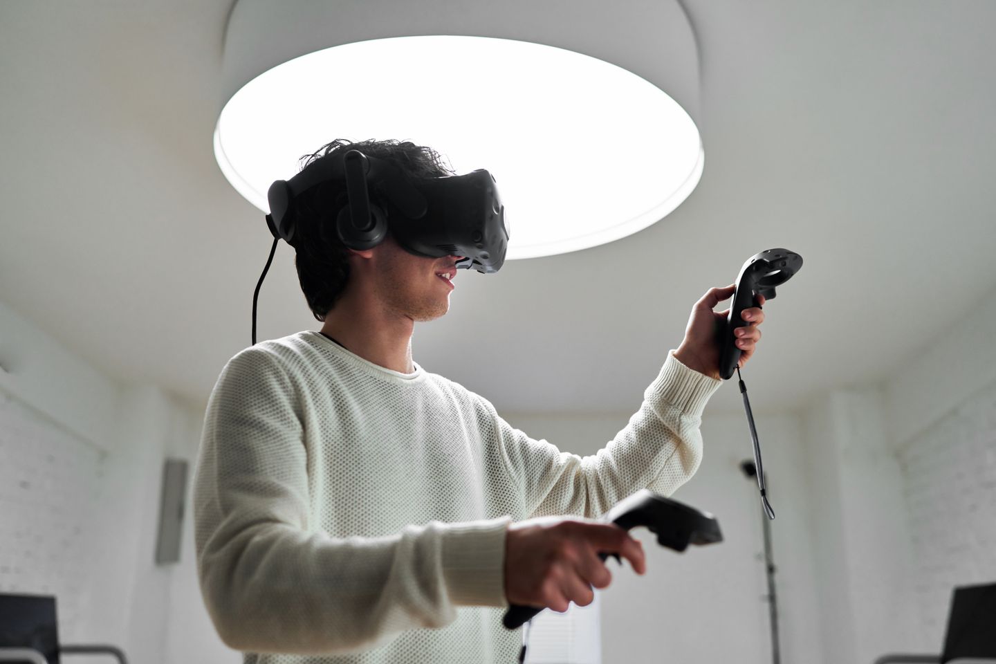 A person using a virtual reality headset and handheld controllers in a bright indoor space